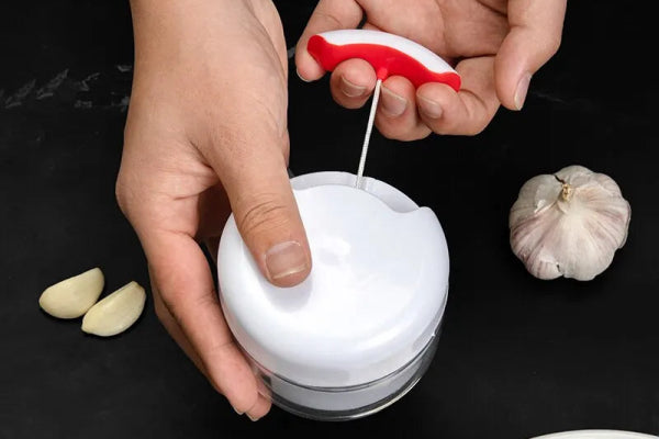 Hand using a white garlic grinder to crush garlic cloves, showcasing the multi-functional design ideal for quick and easy food preparation without knives.