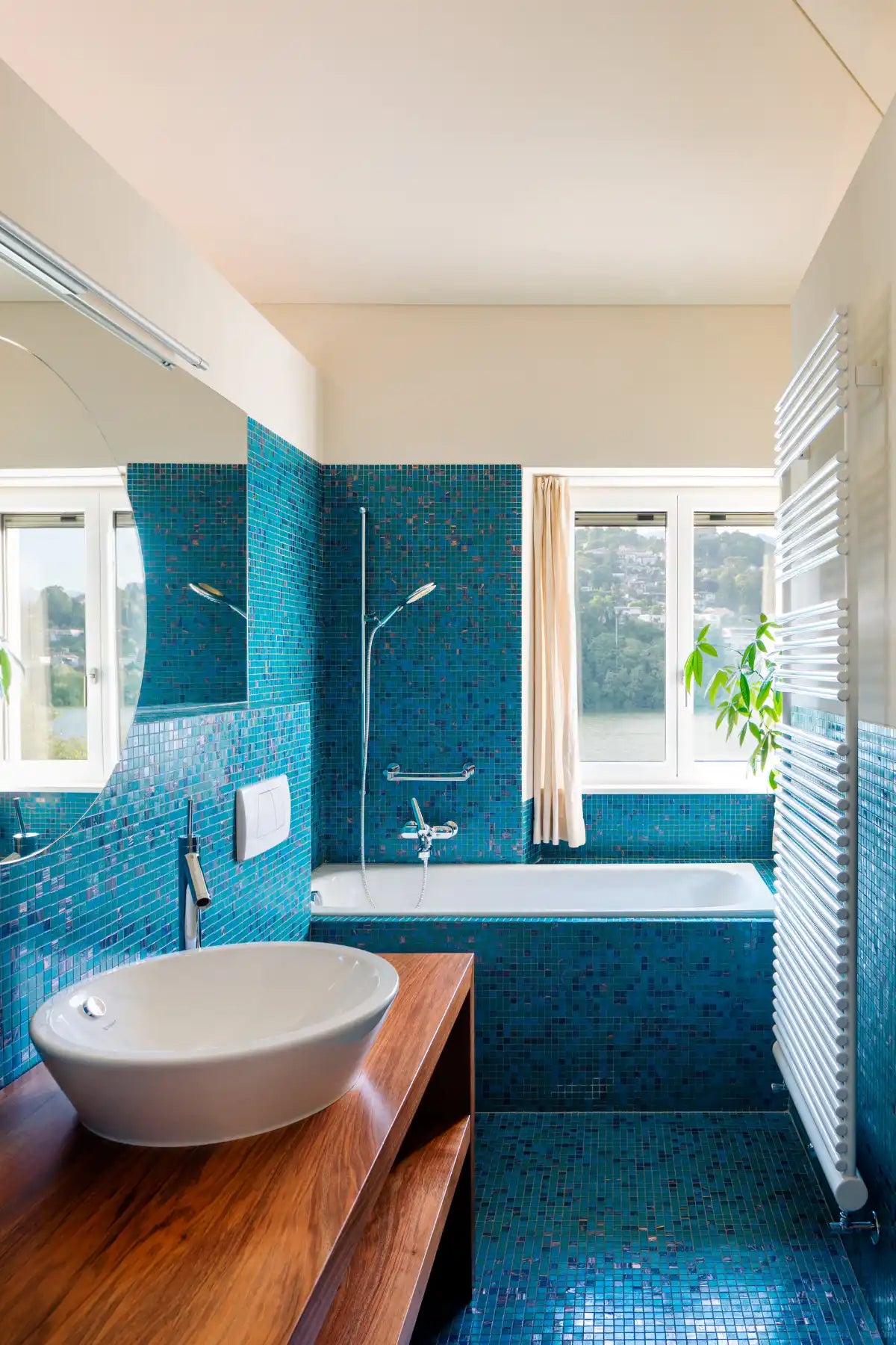 Modern bathroom featuring vibrant turquoise mosaic tiles and a wooden vanity with white vessel sink.