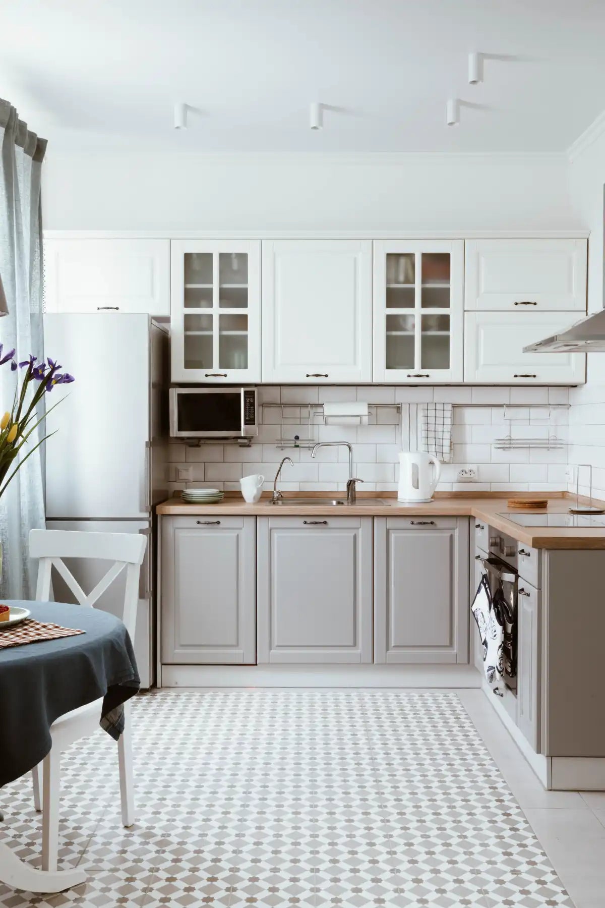 Modern L-shaped kitchen with white upper cabinets and gray lower cabinets featuring wooden countertops.